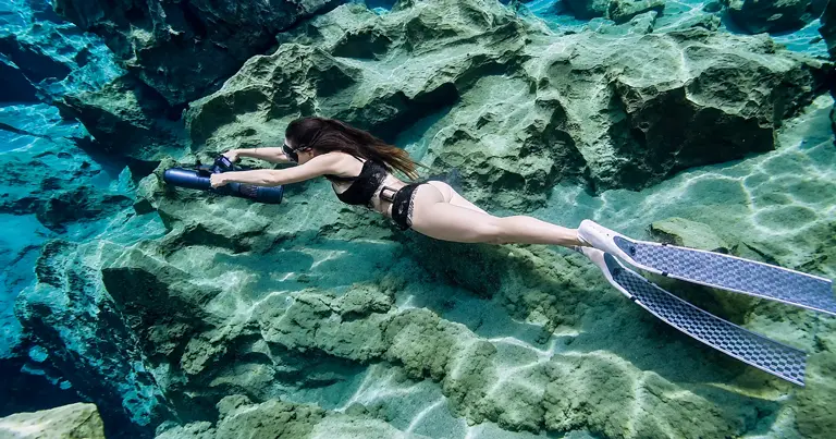 Diver using a KESZING underwater scooter near underwater rocks